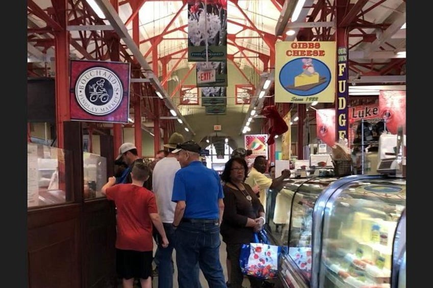 Een markt met bezoekers, borden voor 'Gibb's Cheese' en 'Fudge', en een gekoeld display. 2