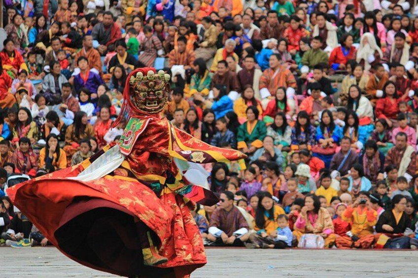 A performer in traditional red attire with a large headdress, performing in front of a crowd. 1