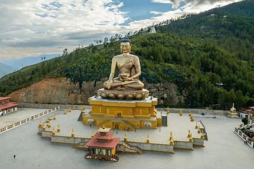 A large seated Buddha statue surrounded by a temple complex with a mountainous backdrop. 2