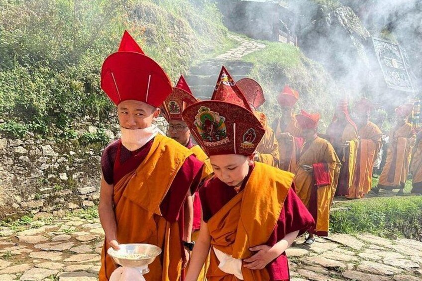 Monks in traditional attire with red hats and yellow robes, standing on a stone path with greenery in the background. 5