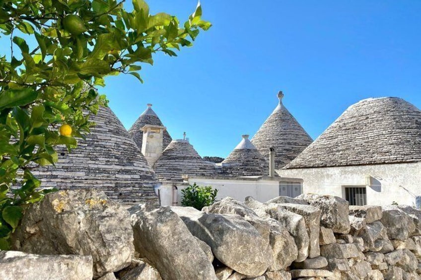Traditional stone houses with conical roofs, a stone wall, and a clear blue sky. 5