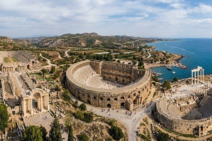 An ancient amphitheater surrounded by ruins and a coastline. 1