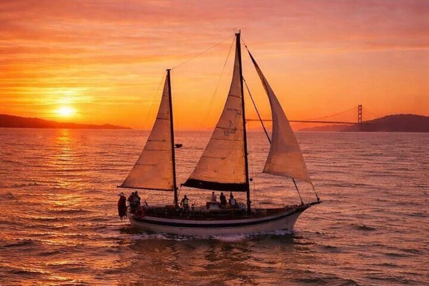 A sailboat on the water during sunset with a bridge in the background. 1