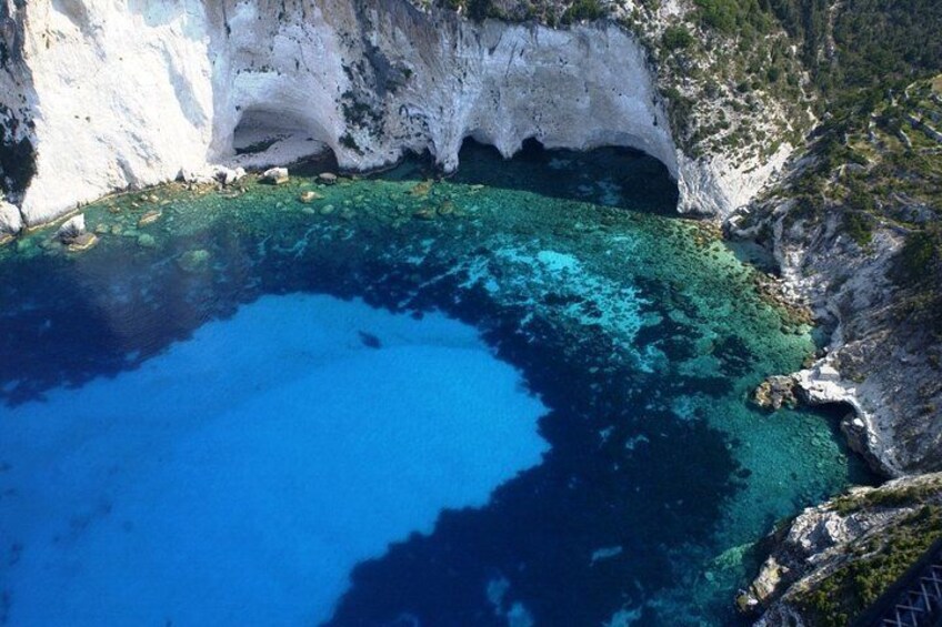 A coastal landscape with a clear blue sea, rocky cliffs, and a small cove. 2