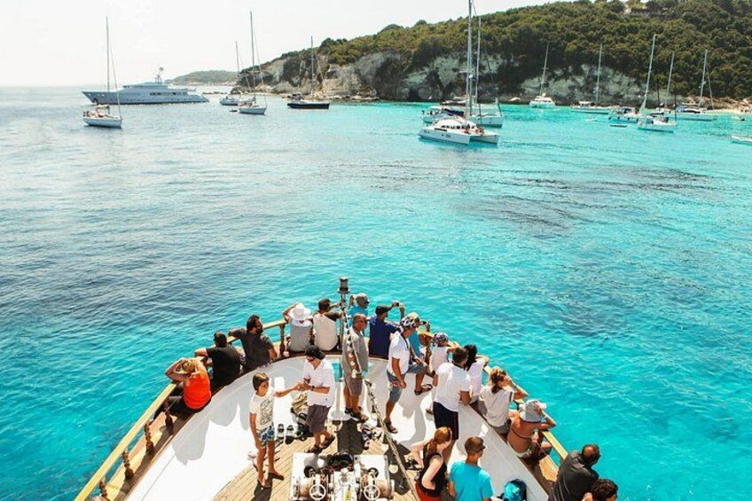 A boat with people on board, surrounded by clear blue water and several sailboats in the distance. 1