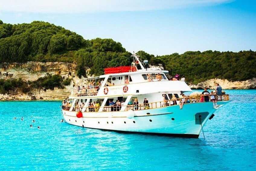 A white boat with passengers on a turquoise sea, surrounded by rocky cliffs and greenery. 3