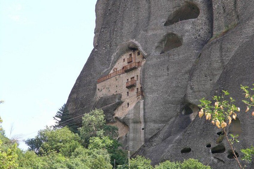 A rock formation with a building carved into it, surrounded by greenery. 1