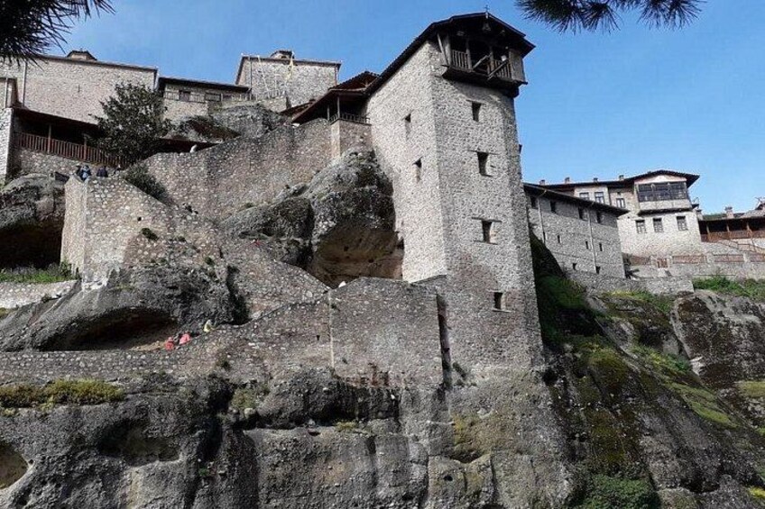 A historic stone fortress with a prominent tower, situated on a rocky outcrop with surrounding buildings. 4