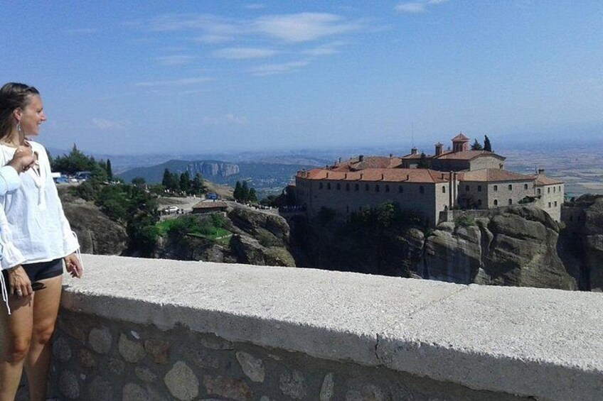A person overlooking a historic building with a red roof, set against a backdrop of rocky terrain and distant cityscape. 5