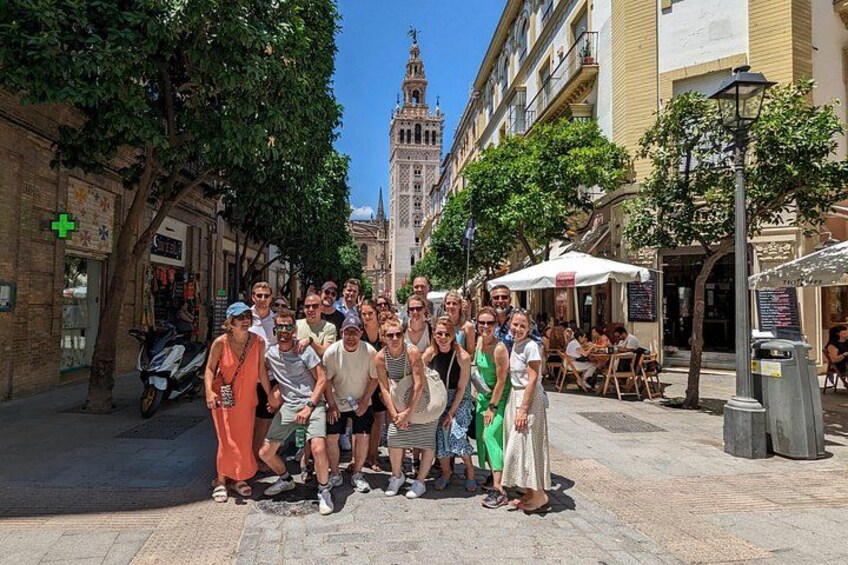 Een groep mensen poseert op een straat in de stad, met historische gebouwen en een toren op de achtergrond. 5