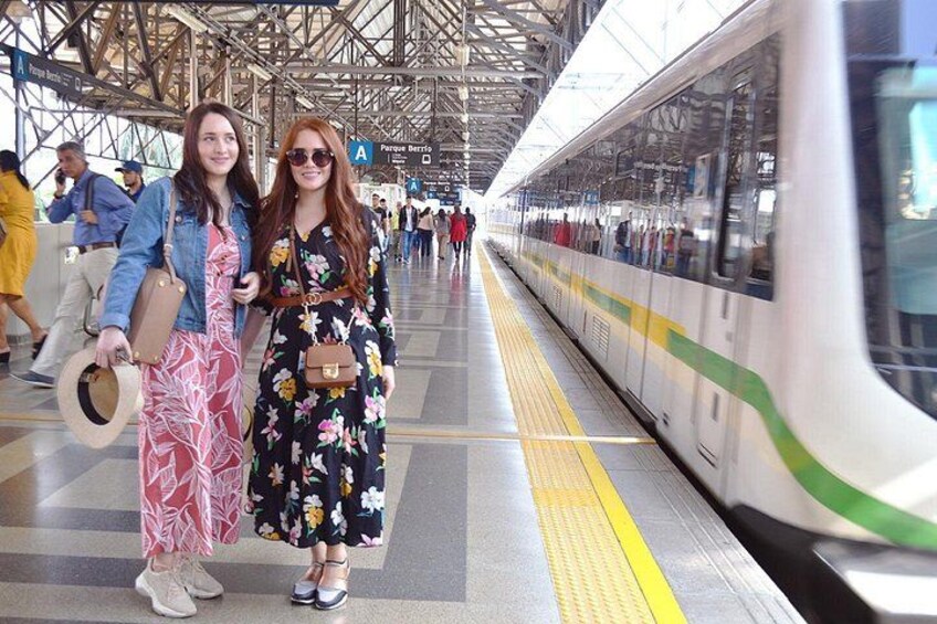 Un andén de estación de tren con un tren, personas y un cartel que indica 'Parque Bernal'. 3