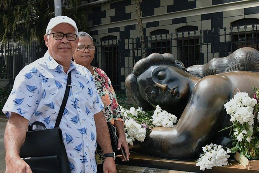 Una escultura de una figura reclinada con flores, un edificio con ventanales arqueados y una valla de fondo. 5