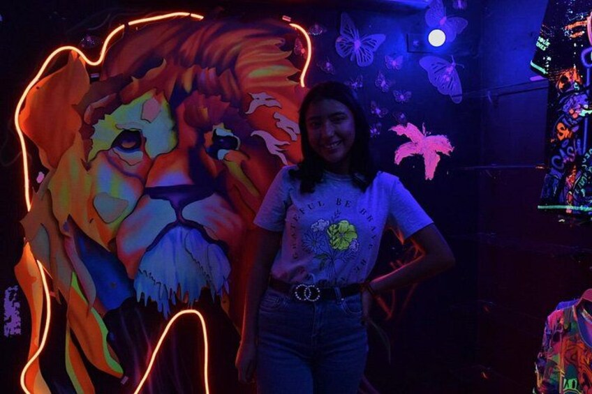 Una persona de pie frente a un mural iluminado con un león de neón. 5