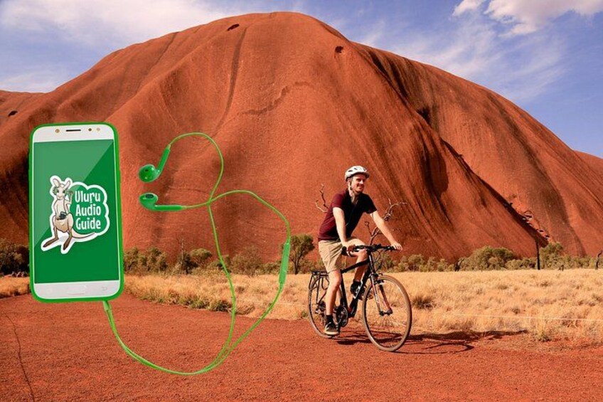 A person riding a bicycle in front of Uluru with a smartphone displaying the Uluru Audio Guide. 2