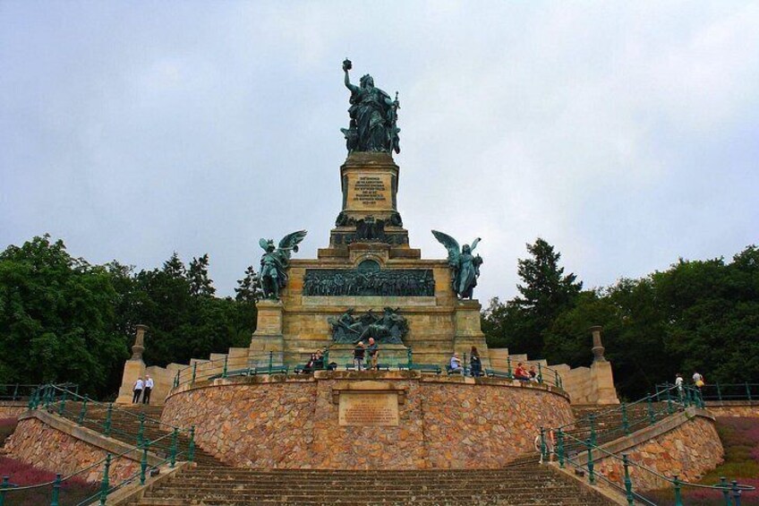 Una estatua grande sobre un pedestal con escalones que llevan hasta ella, rodeada de follaje. 3