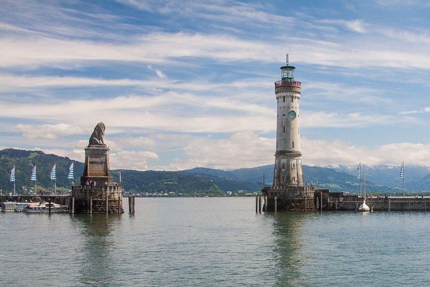 Un faro y una estatua en un muelle, con un lago tranquilo y montañas al fondo. 2