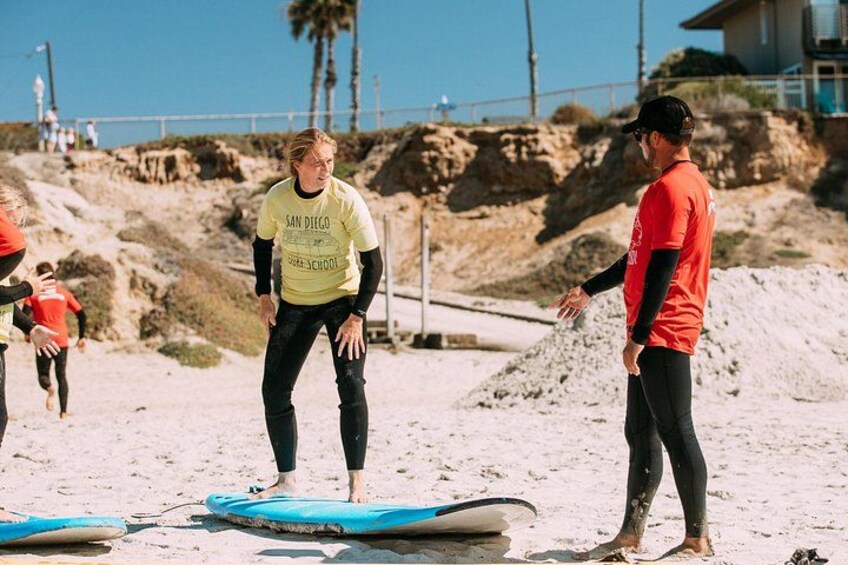 A beach with people standing on surfboards, a lifeguard tower in the background, and a clear sky. 4