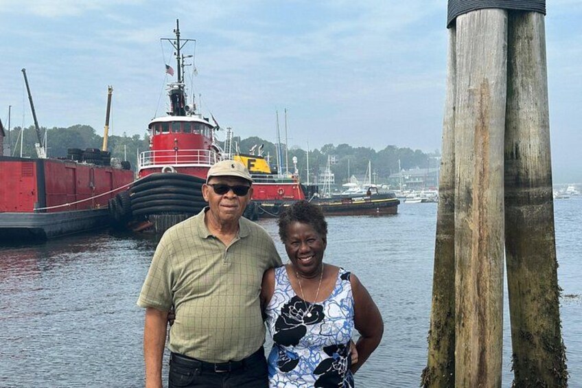 Two people standing by a dock with a red ship in the background. 4