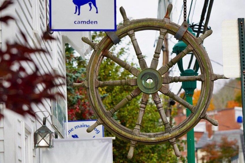 A ship's wheel mounted on a building, a sign with a cow symbol, and a banner with text. 1