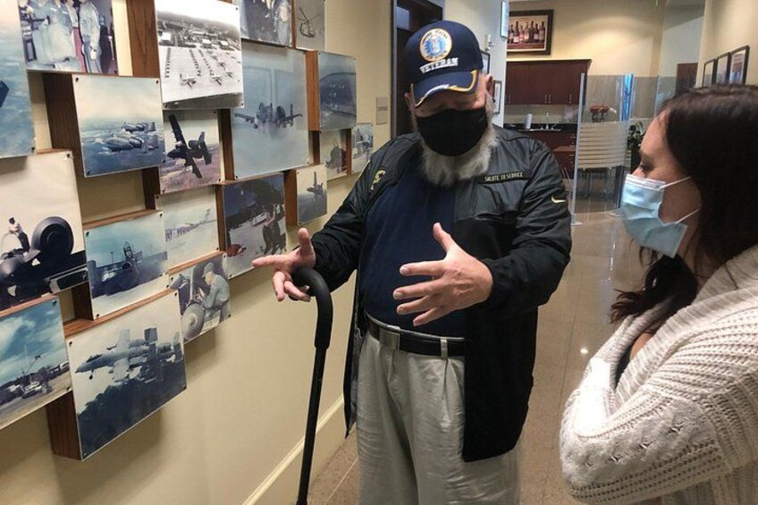 A person gesturing towards a wall of military aircraft paintings. 4