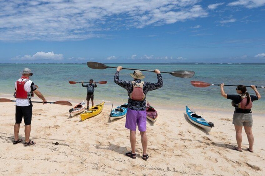 Three people on a beach with kayaks and paddles, preparing for kayaking. 2