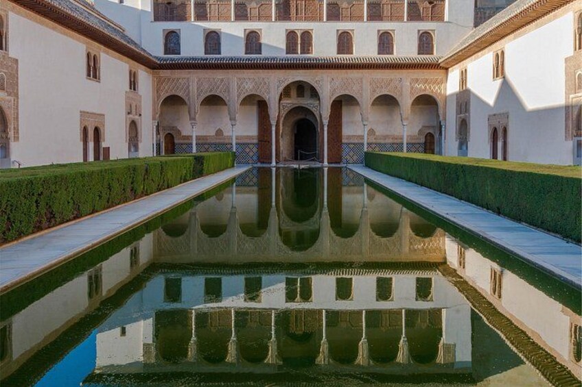 Un patio con piscina central, paseos con arcos y un edificio con balcones ornamentados. 2