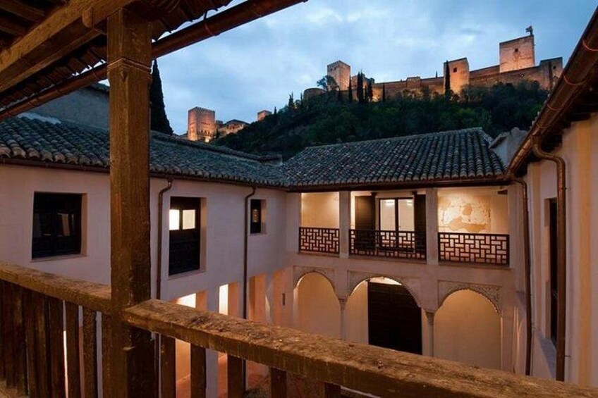 A courtyard with a wooden railing, a building with a tiled roof, and a castle in the background. 4