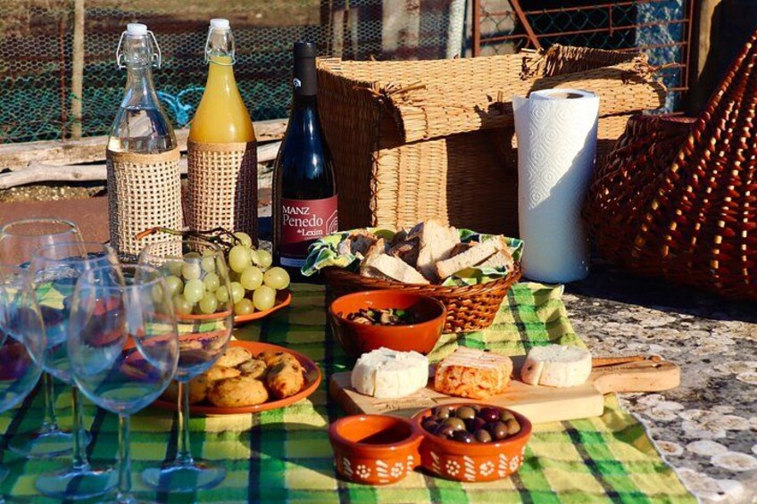 Een picknickopstelling met wijnflessen, glazen, brood, kaas, olijven en een mand op een tafel. 2