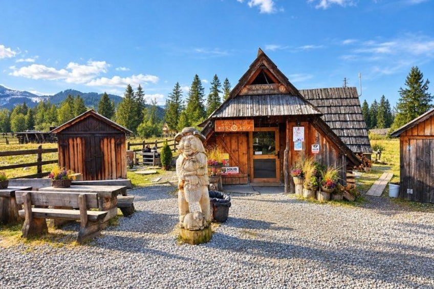 A wooden building with a sloped roof, surrounded by a gravel area and a wooden fence. 2