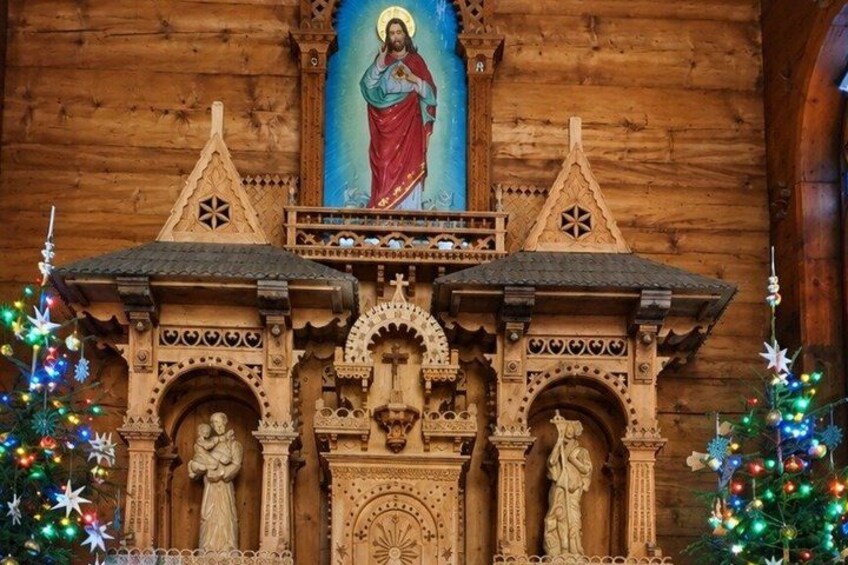 Una struttura in legno con statue religiose e un dipinto, circondata da alberi di Natale. 5
