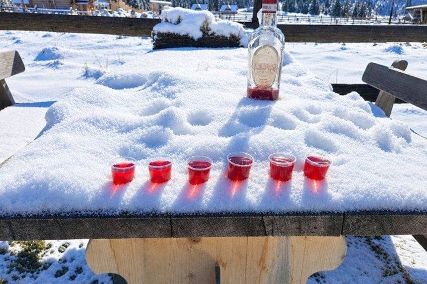 Un tavolo di legno con una bottiglia e bicchieri rossi, circondato dalla neve. 3