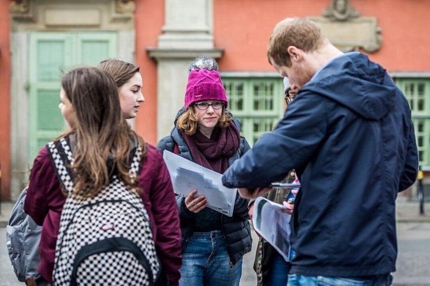 A group of people standing outdoors, some holding papers, in front of a building with green doors. 4