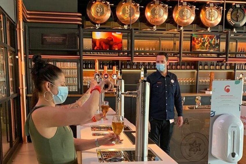 Een bartender schenkt een drankje in, een man staat achter de bar en koperen bierkraaninstallaties op de achtergrond. 5
