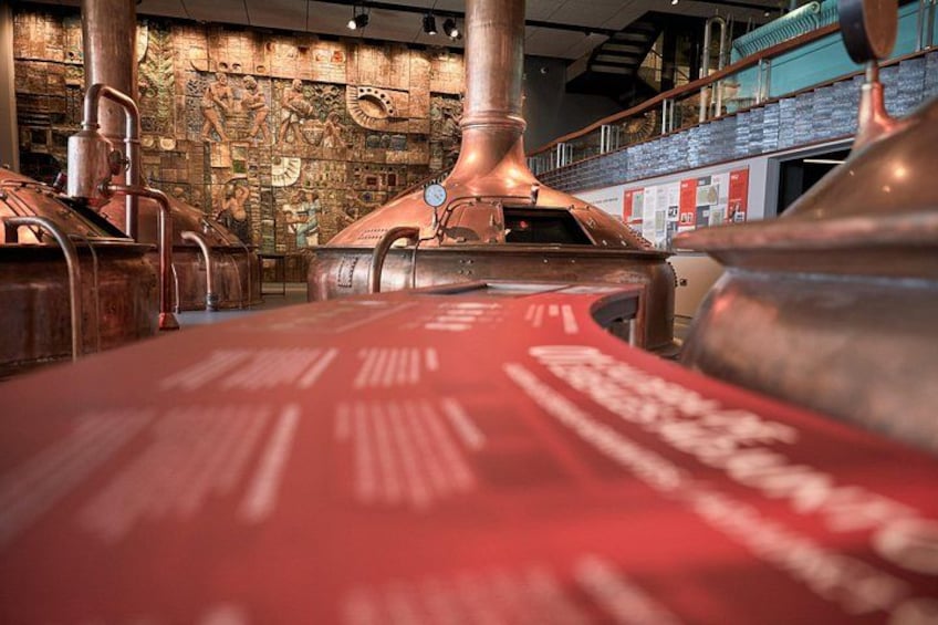 Interieur van een distilleerderij met koperen brouwapparatuur en een rood transportband. 4