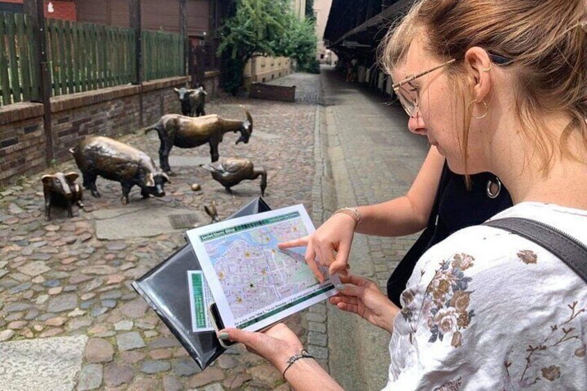 A person using a tablet with a map in a cobblestone area with animal statues. 3