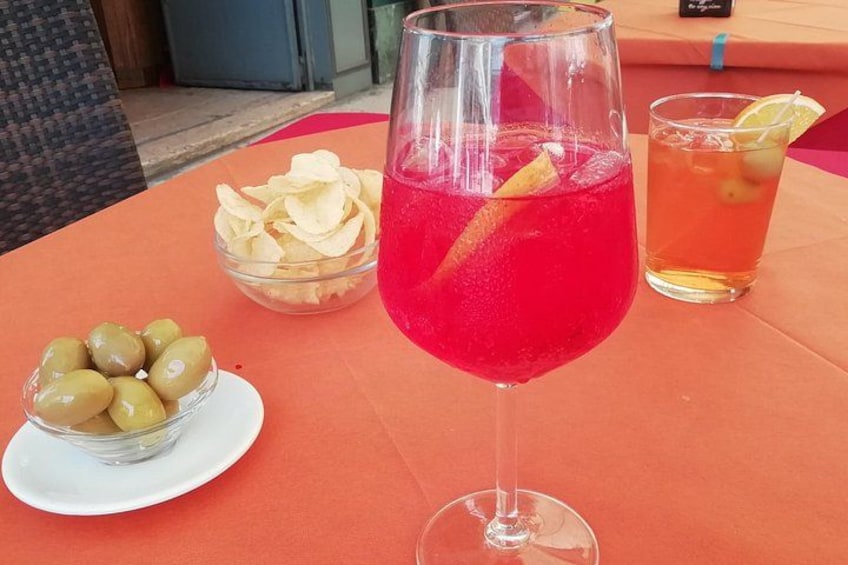 Una mesa con una bebida roja, una taza de té, papas fritas y aceitunas. 1