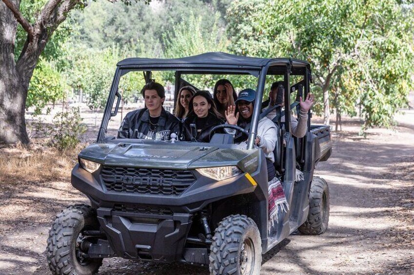 A Polaris RZR off-road vehicle with four passengers, parked on a dirt path surrounded by trees. 5