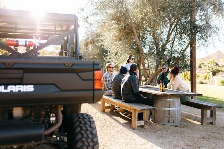 A group of people sitting at a wooden picnic table outdoors with a Polaris vehicle in the foreground. 4