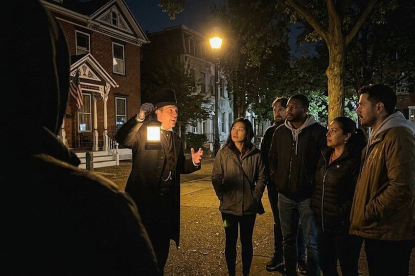 A group of people standing on a street at night, with a house and street lamps in the background. 2
