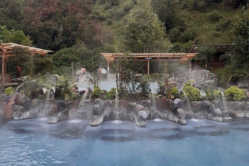 A hot spring area with multiple small waterfalls and a wooden structure in the background. 1