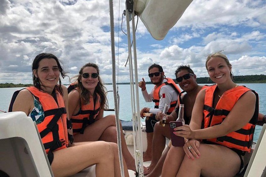 A group of people on a boat wearing life jackets, with a body of water and a cloudy sky in the background. 4