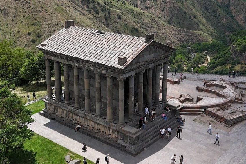 An ancient temple with columns, surrounded by a mountainous landscape. 1