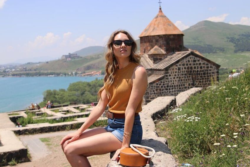 A person sitting on a stone ledge overlooking a body of water, with a church and hills in the background. 1
