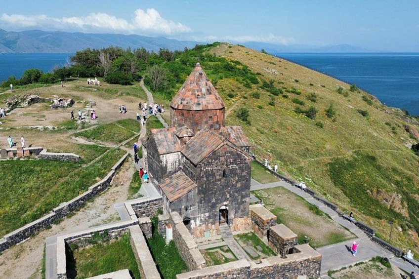 A historical building with a conical roof, surrounded by a grassy area with pathways and visitors. 4