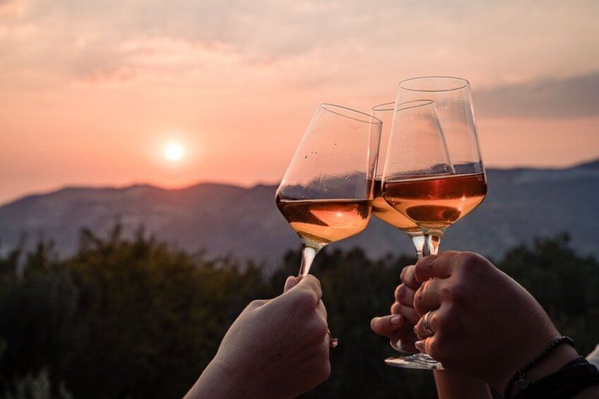 Zwei Personen stoßen mit Weingläsern bei einem Sonnenuntergang über den Bergen an. 1