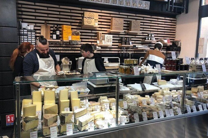 A cheese shop with a glass display case filled with various cheeses. 4