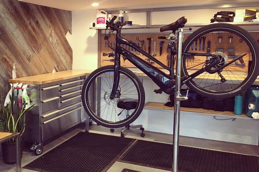 A bicycle mounted on a stand in a room with a wooden wall, a pegboard with tools, and a counter with drawers. 1