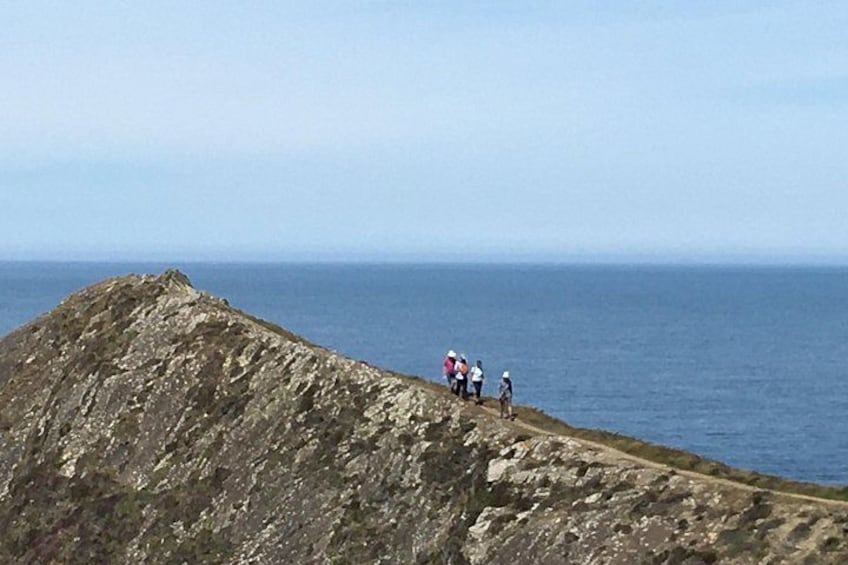 Costa rocosa con un grupo de personas de pie en un acantilado, con vista al mar. 2