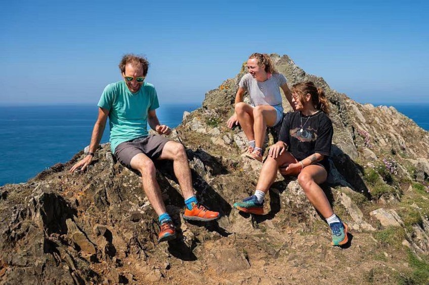 Tres personas sentadas sobre un saliente rocoso con vista al océano. 5
