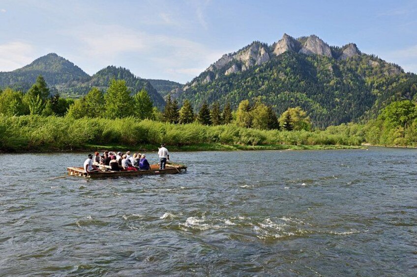 Un grupo de personas en un bote de madera en un río, rodeado de colinas y montañas verdes y frondosas. 3